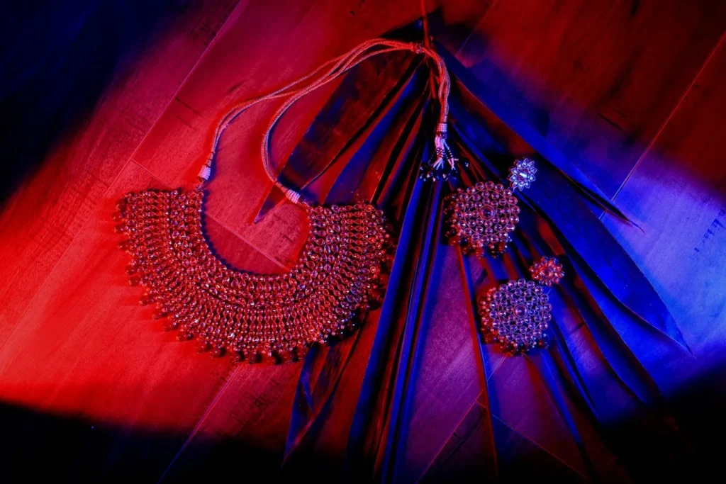 Red bridal necklace and earrings laid out on silk under red and blue light, bridal jewellery detail photograph