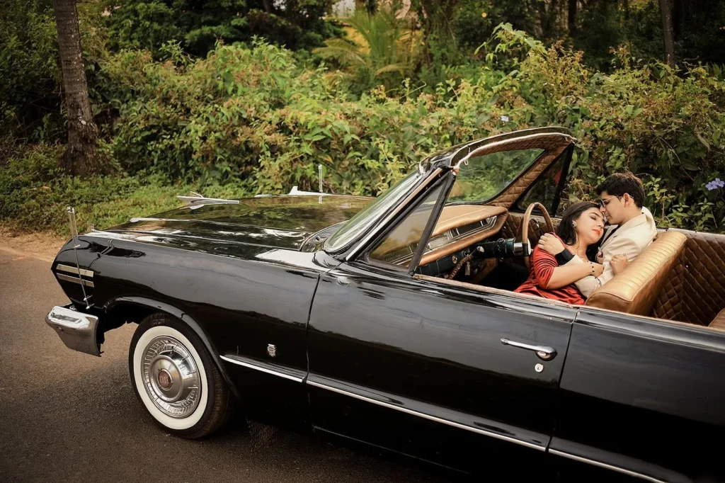 Couple sitting together in a black vintage convertible car on a tree-lined road for a pre-wedding shoot