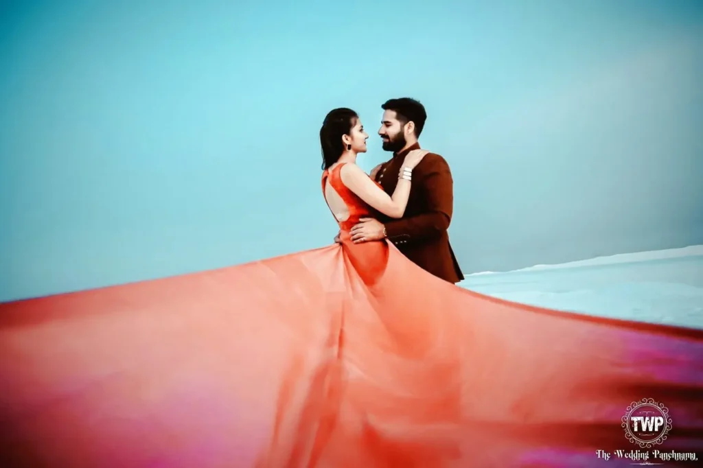 Couple in red gown and brown sherwani against a pastel sky, pre-wedding shoot location in Indore