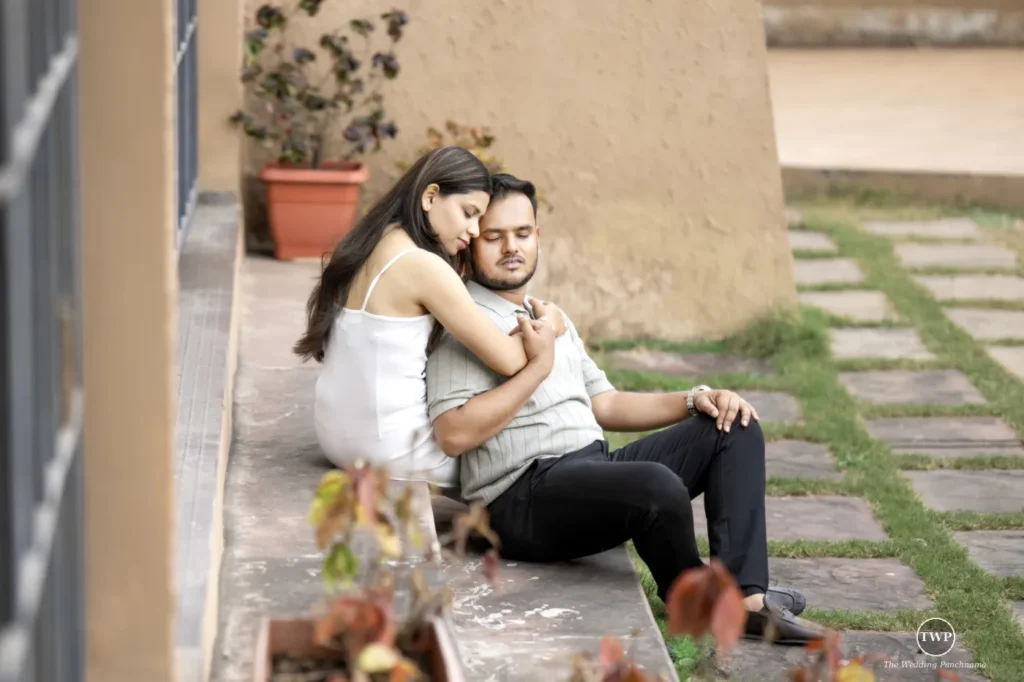 A couple sitting close on the steps of a sunlit courtyard, the woman in white resting her head near the man's shoulder