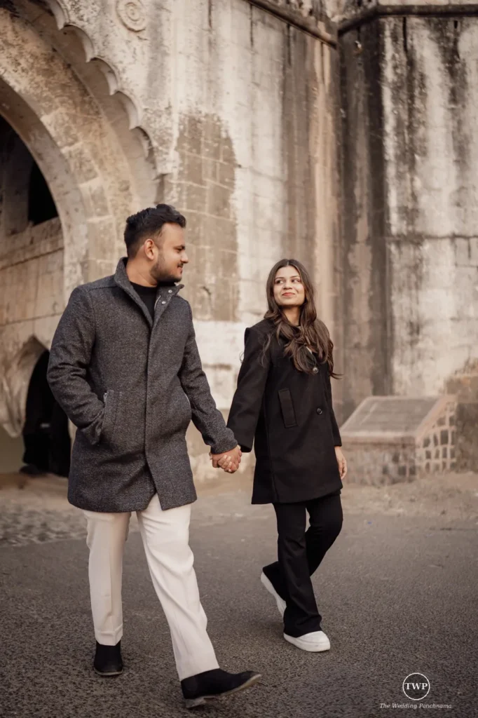 Couple in winter coats walking hand in hand at a heritage stone location on their pre-wedding shoot