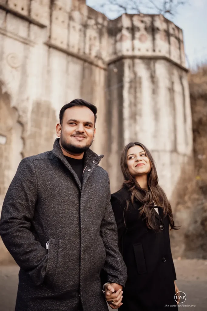 Smiling couple with styled hair holding hands at an old stone monument during their pre-wedding shoot