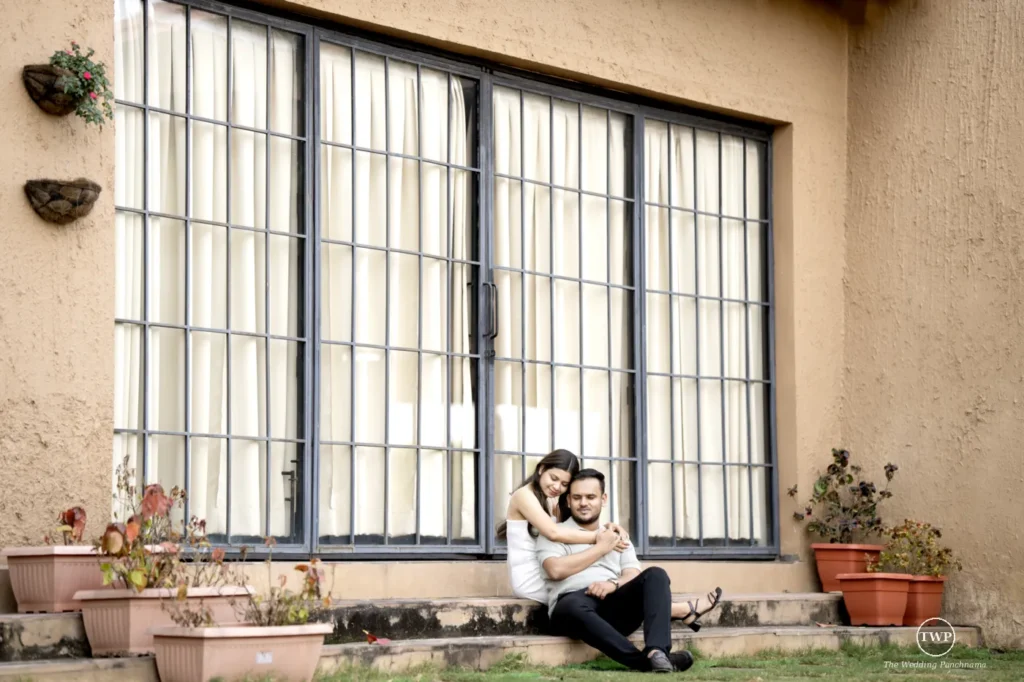 Couple sitting together on farmhouse veranda steps before a large grid window during their pre-wedding shoot near Indore